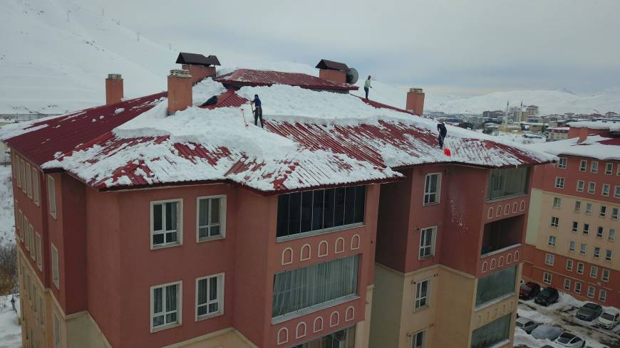 Bellerine bağladıkları iplerle çatılardan kar temizliyorlar